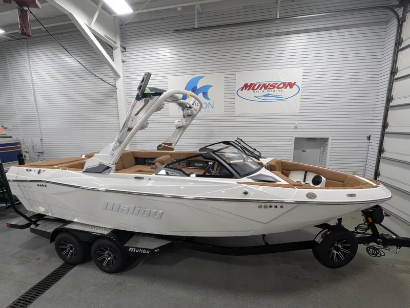 The Image of 2026 Malibu 23 LSV boat in showroom, white exterior, tan interior, on trailer. - 0