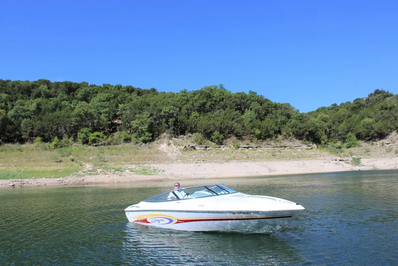 Slide: The Image of 2002 Baja 232 boat on a serene lake with lush green shoreline. - 10