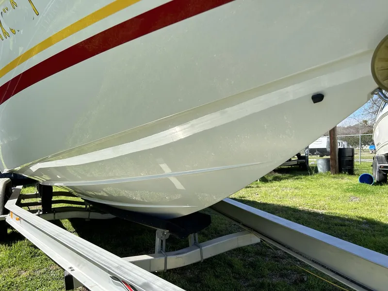 Slide: The Image of 2002 Baja 232 boat on trailer, white hull with red and yellow stripes, parked on grass. - 16