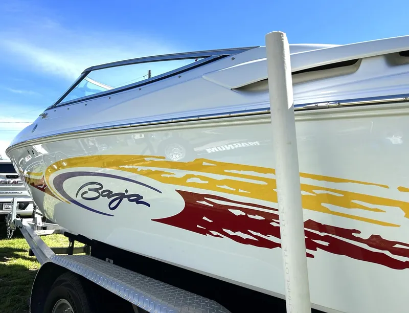 Slide: The Image of 2002 Baja 232 boat with colorful graphics on a trailer under a clear blue sky. - 20