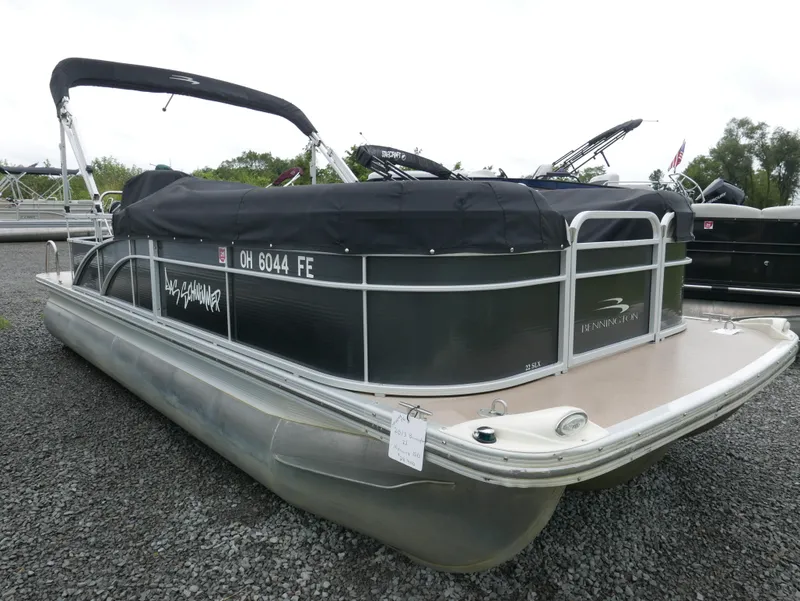 Slide: The Image of 2013 Bennington 22SLX pontoon boat with black cover, parked on gravel. - 2