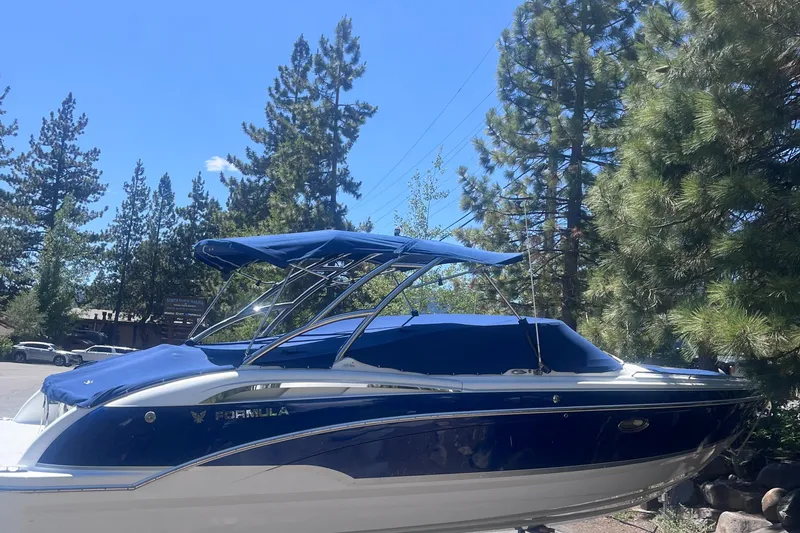 Slide: The Image of 2008 Formula 310 Bowrider boat with blue canopy, parked near pine trees. - 1