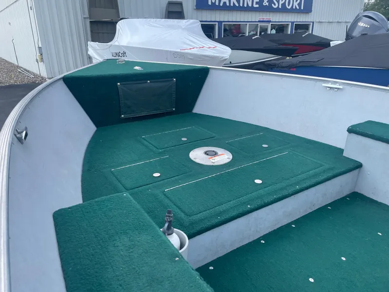 Slide: The Image of 2003 Lund 1650-V Rebel Tiller boat interior with green carpet, parked at a marine store. - 17