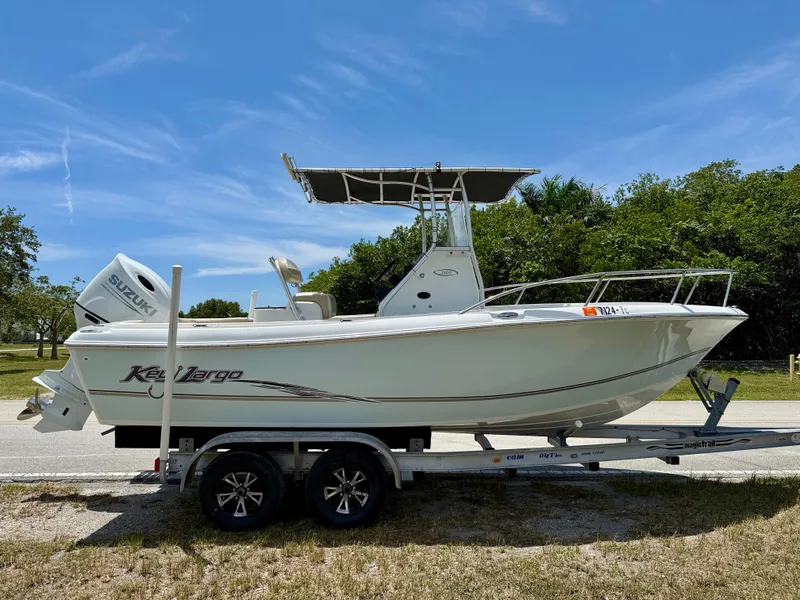 Slide: The Image of 2016 Key Largo 2100 WI CC boat on trailer, clear sky, lush greenery background. - 2