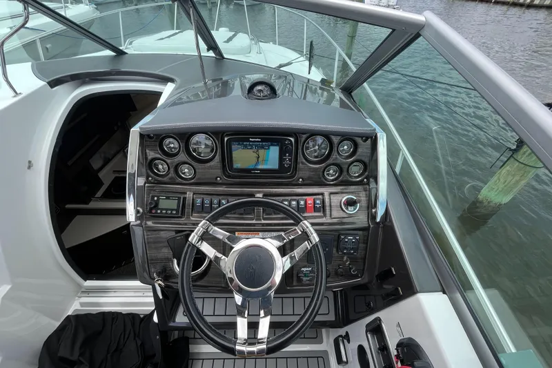 Slide: The Image of 2016 Monterey 295 Sport Yacht helm with navigation system and steering wheel, docked by the water. - 15