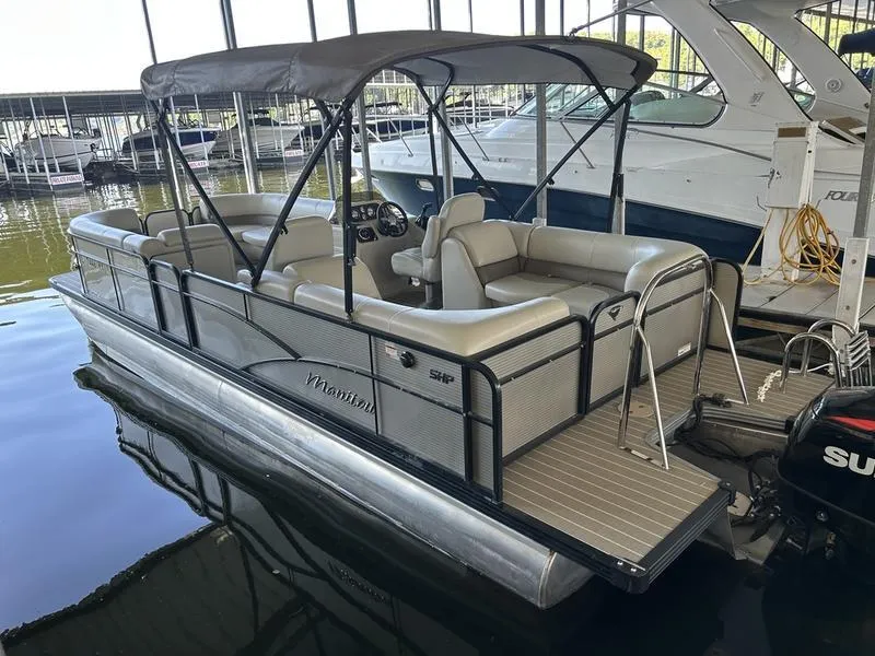Slide: The Image of 2019 Manitou 250 SHP pontoon boat docked in marina, featuring spacious seating and canopy. - 2