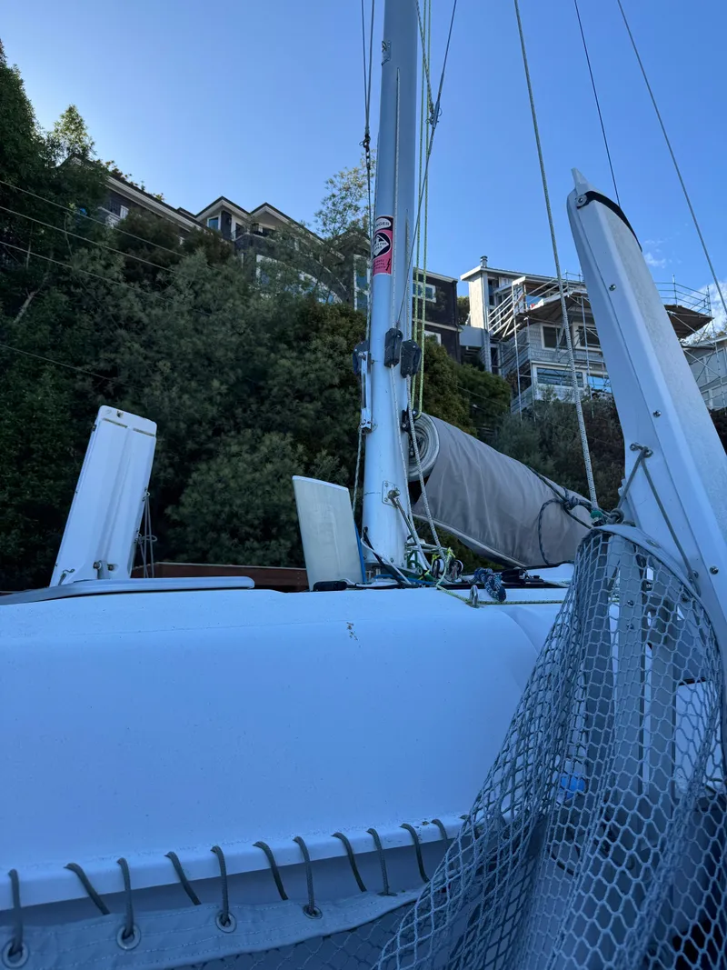 Slide: The Image of 2018 Corsair 760 Sport sailboat with mast and rigging, docked near hillside homes. - 11