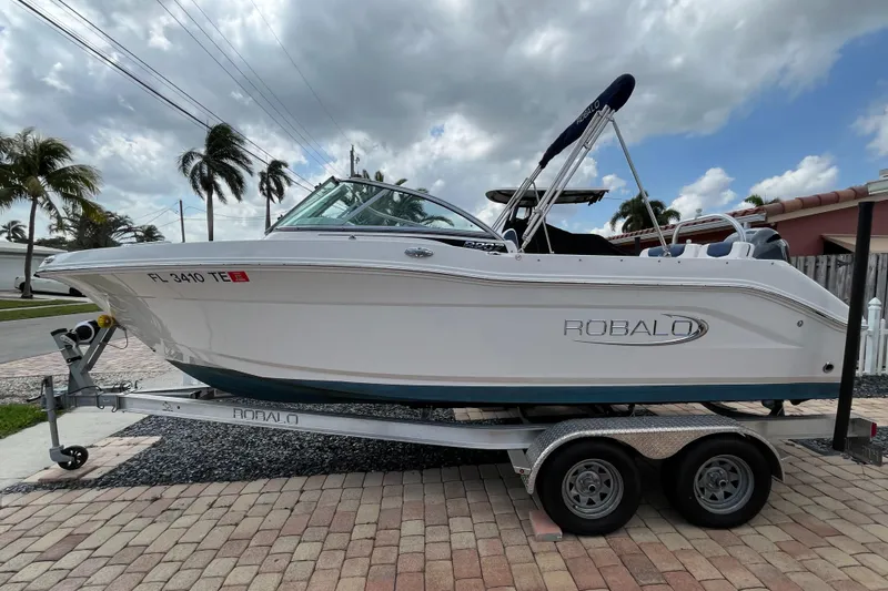 Slide: The Image of 2021 Robalo 207R boat on trailer, parked on brick driveway under cloudy sky. - 0