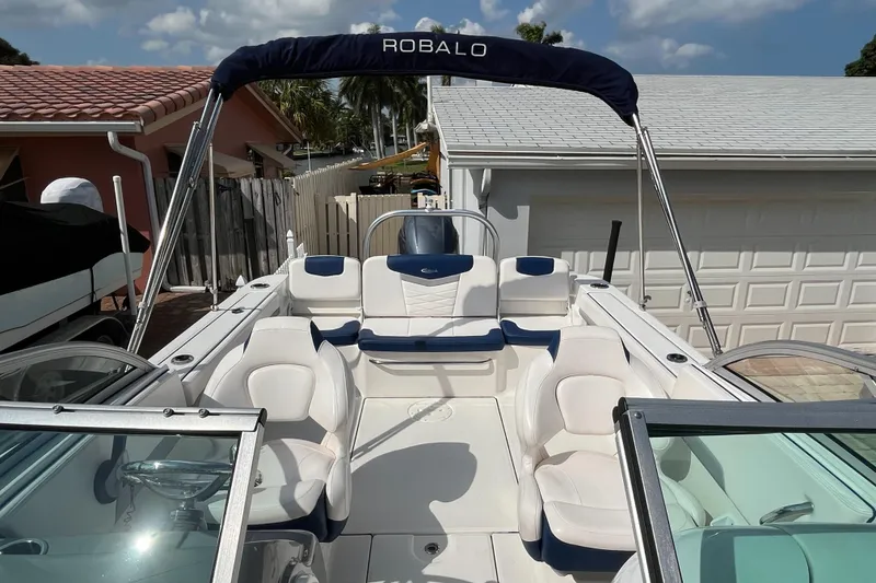 Slide: The Image of 2021 Robalo 207R boat with white and blue seating, parked in a driveway. - 2
