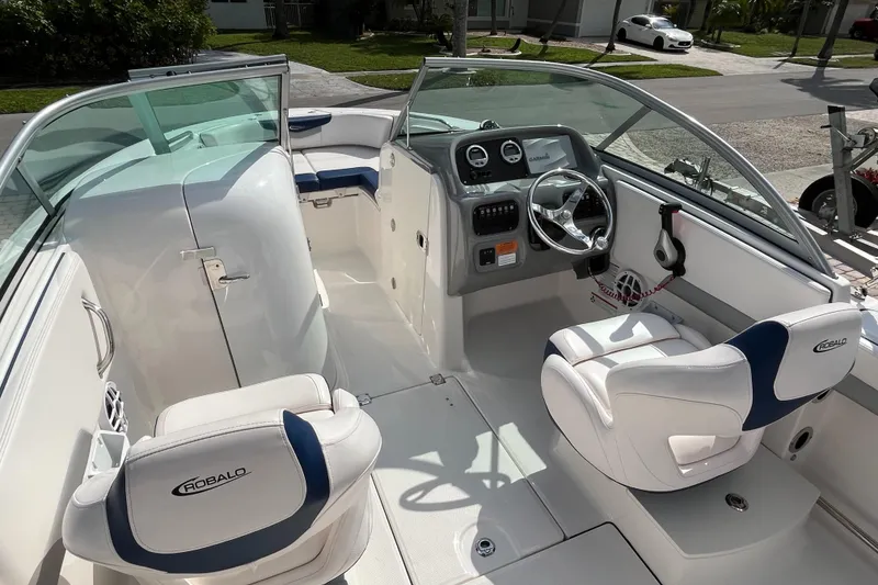 Slide: The Image of 2021 Robalo 207R boat interior with steering wheel and seating, parked on a sunny day. - 5