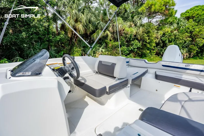 Slide: The Image of 2021 Hurricane SunDeck Sport 205 OB boat interior with seating and steering, surrounded by lush greenery. - 6