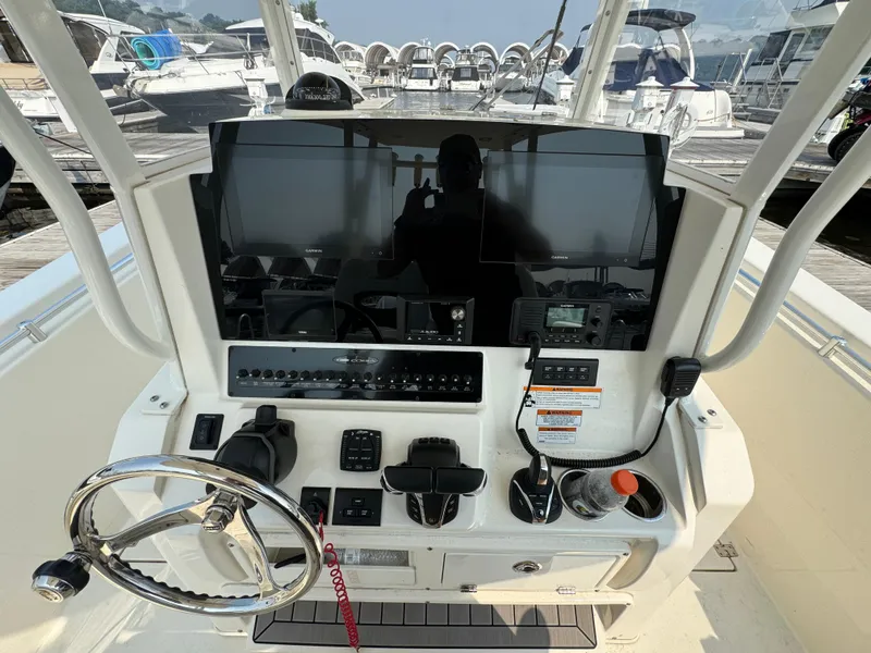 Slide: The Image of 2023 Cobia 301 CC boat dashboard with steering wheel and navigation controls at marina. - 13