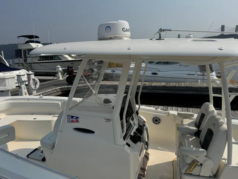Slide: The Image of 2023 Cobia 301 CC boat at marina, featuring helm and seating area. - 23
