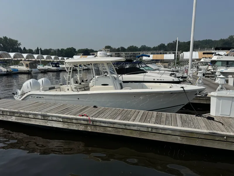 Slide: The Image of 2023 Cobia 301 CC boat docked at a marina with other vessels. - 4