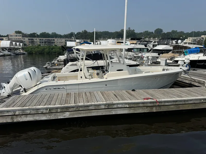 Slide: The Image of 2023 Cobia 301 CC boat docked at marina, featuring twin outboard engines. - 5