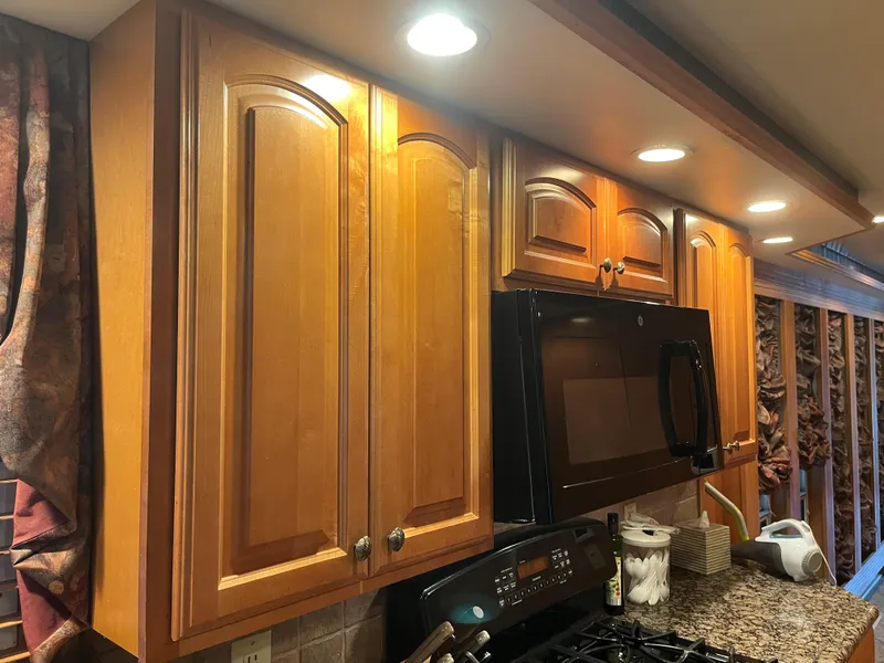 Slide: The Image of Wooden kitchen cabinets with under-cabinet lighting above a black microwave and granite countertop. - 24