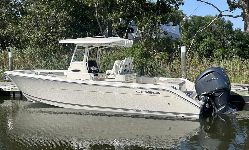 The Image of 2026 Cobia 285 Center Console boat docked by lush greenery. - 0