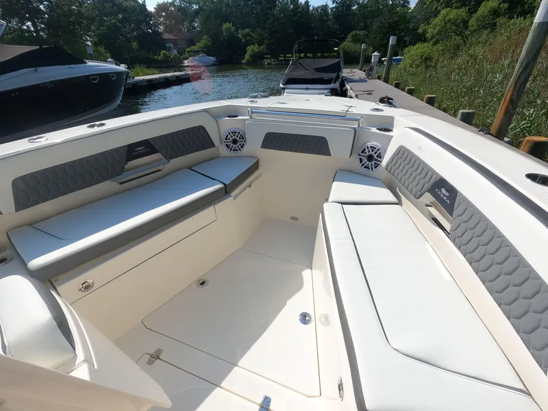 Slide: The Image of 2026 Cobia 285 Center Console boat interior with cushioned seating and speakers, docked by a serene lake. - 16