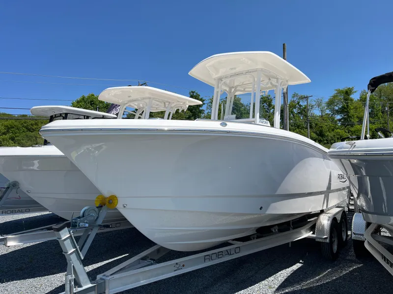 The Image of 2024 Robalo R230 Center Console boat on trailer, under clear blue sky. - 0
