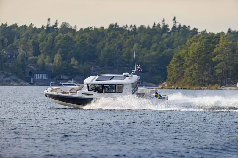 Slide: The Image of 2025 Nimbus Commuter 9 boat cruising on a scenic lake with forested shoreline. - 2