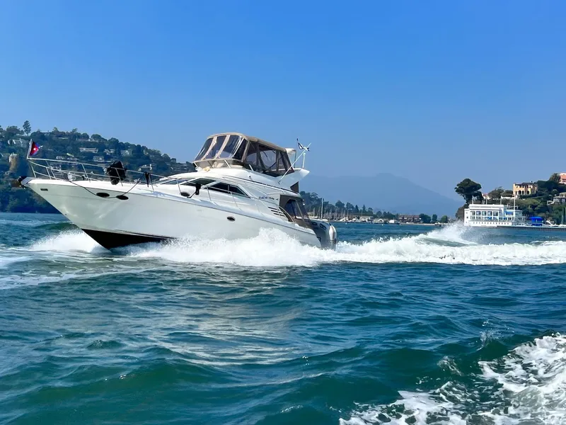 The Image of 1997 Sea Ray 400 Sedan Bridge cruising on a sunny day, with scenic coastal backdrop. - 0