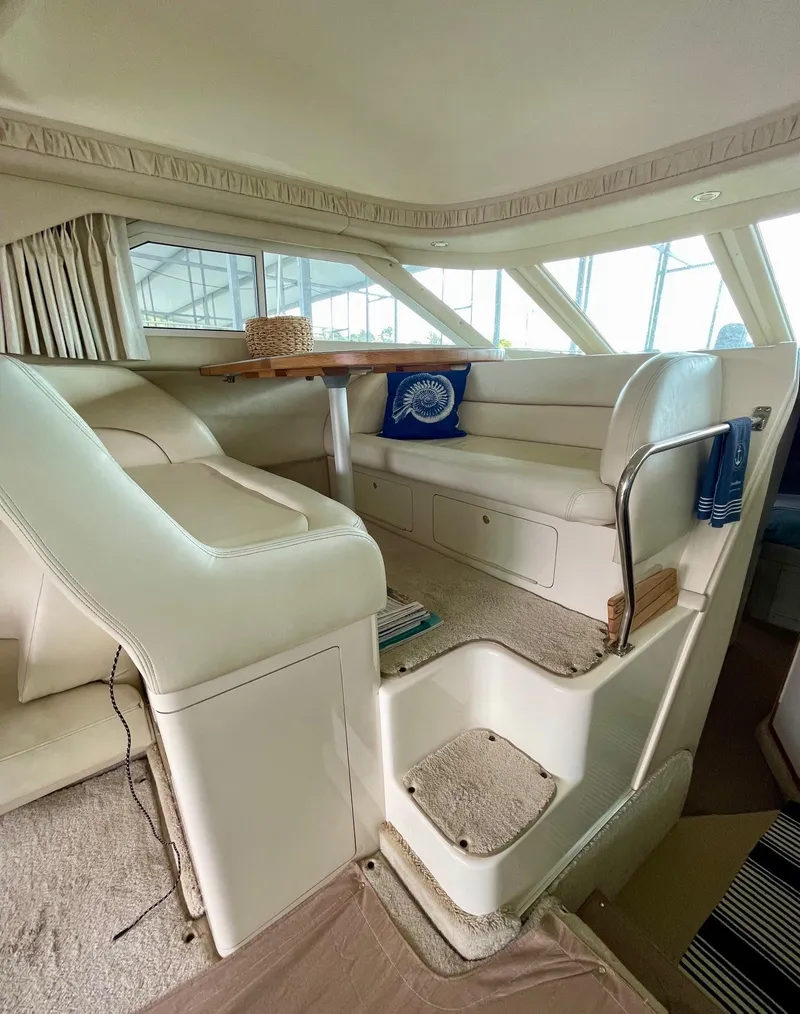 Slide: The Image of Interior of 1997 Sea Ray 400 Sedan Bridge with white seating and wooden table. - 12