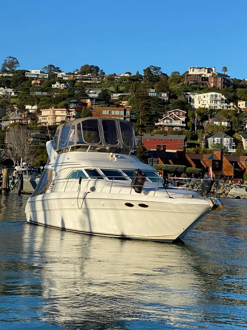 Slide: The Image of 1997 Sea Ray 400 Sedan Bridge yacht on calm water, with hillside homes in the background. - 2