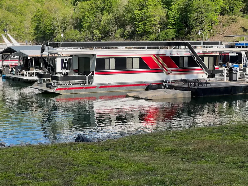 The Image of 1993 Sumerset houseboat docked on a serene lake with lush green surroundings. - 2