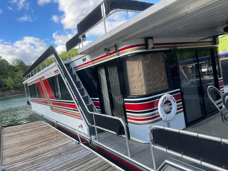 Slide: The Image of 1993 Sumerset houseboat docked, featuring red and black stripes, under a partly cloudy sky. - 34