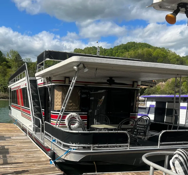 Slide: The Image of 1993 Sumerset houseboat docked, featuring outdoor seating and scenic background. - 5