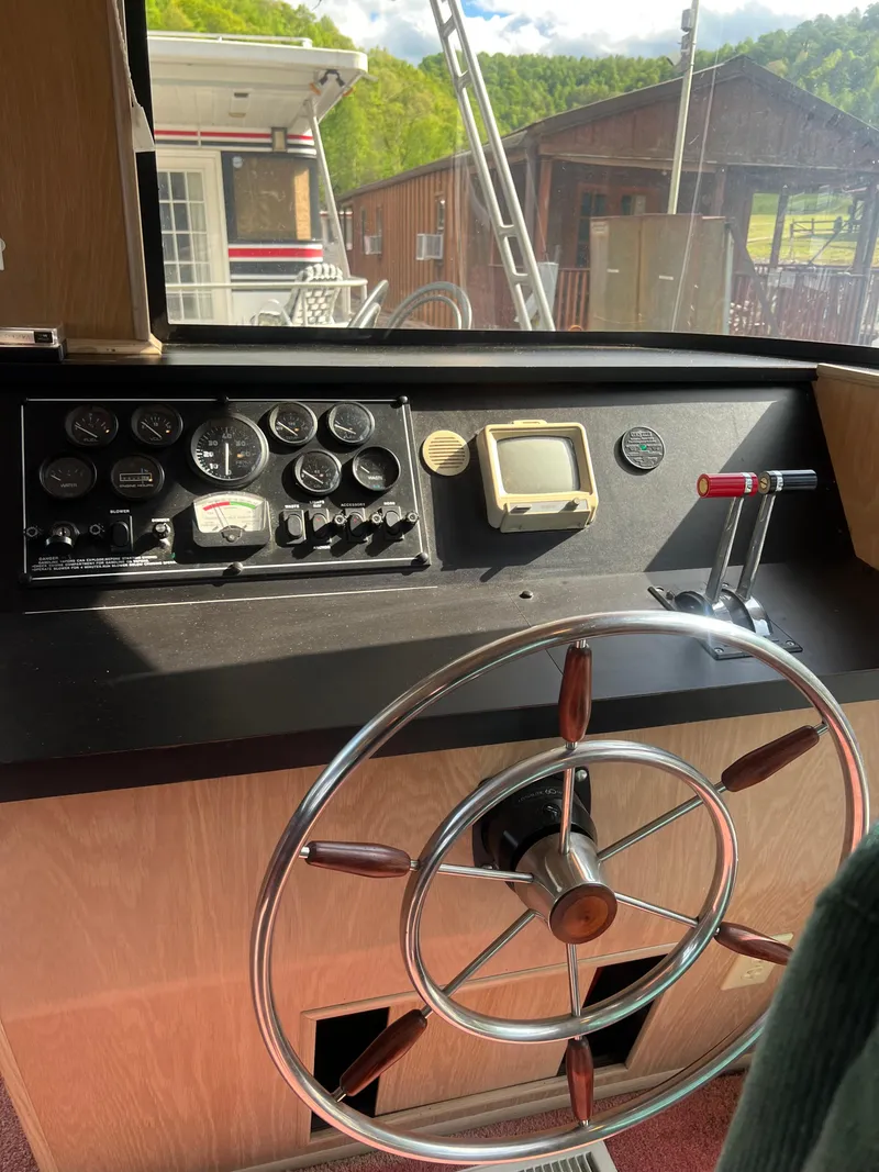Slide: The Image of 1993 Sumerset houseboat helm with steering wheel, gauges, and controls, docked near wooden buildings. - 9