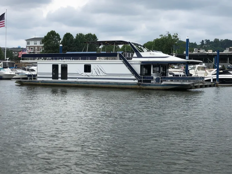 The Image of 1997 Sumerset 75' X 16' houseboat docked on a calm river under cloudy skies. - 0