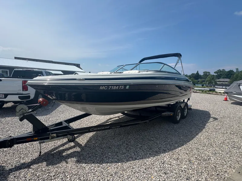 Slide: The Image of 2014 Crownline 235 SS boat on trailer, parked on gravel lot under clear sky. - 2
