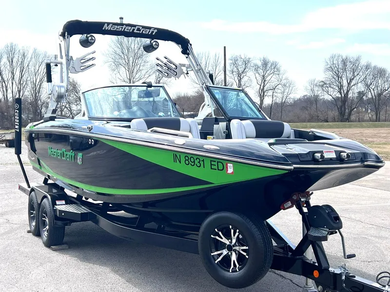 Slide: The Image of 2015 MasterCraft X25 boat with green accents on a trailer, parked outdoors. - 2