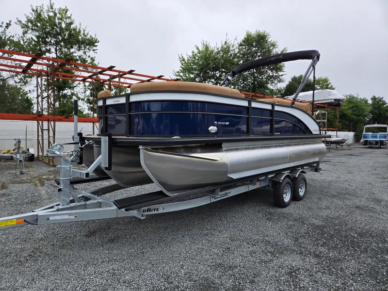 The Image of 2026 Harris Cruiser 210 pontoon boat on a trailer, parked on gravel. - 0