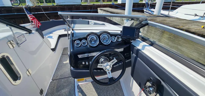 Slide: The Image of 2014 Glastron GT 245 boat dashboard with steering wheel and gauges, docked with American flag. - 15