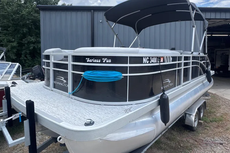 Slide: The Image of 2023 Bennington 22SX Swingback pontoon boat with canopy, docked near a metal building. - 0