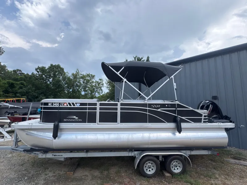 Slide: The Image of 2023 Bennington 22SX Swingback pontoon boat on trailer, under cloudy sky. - 2