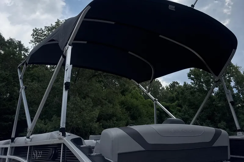 Slide: The Image of 2023 Bennington 22SX SWINGBACK pontoon boat with canopy, set against a wooded backdrop. - 5
