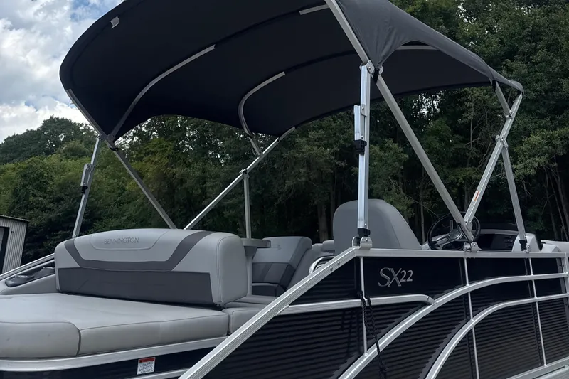 Slide: The Image of 2023 Bennington 22SX Swingback pontoon boat with canopy, parked near trees. - 8
