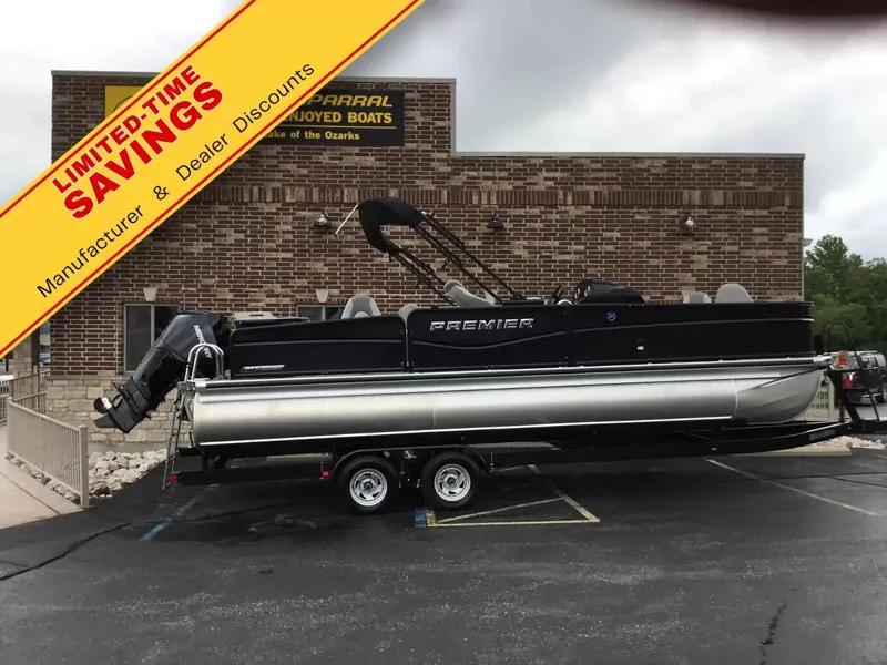 The Image of 2024 Premier 230 Sunsation Angler 4pt pontoon boat on a trailer, parked in front of a building. - 1