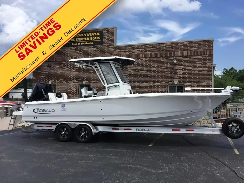 The Image of A Robalo 266 Cayman boat on a trailer in front of a brick building with a promotional banner. - 1