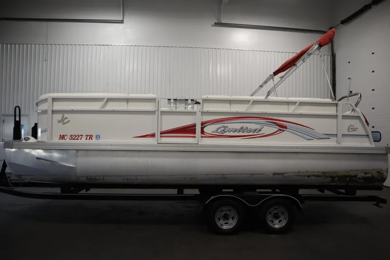 Slide: The Image of 2014 JC 22 Limited pontoon boat with red accents, displayed indoors on a trailer. - 7