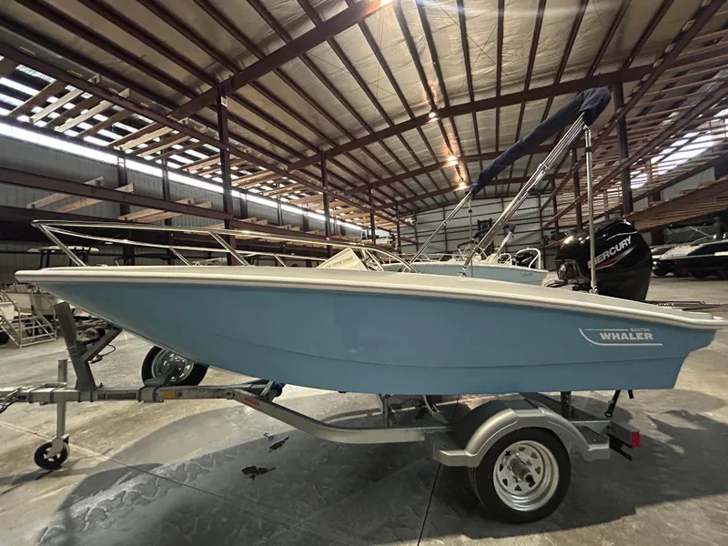 Slide: The Image of 2026 Boston Whaler 130 Super Sport boat in storage, blue hull, on trailer. - 8