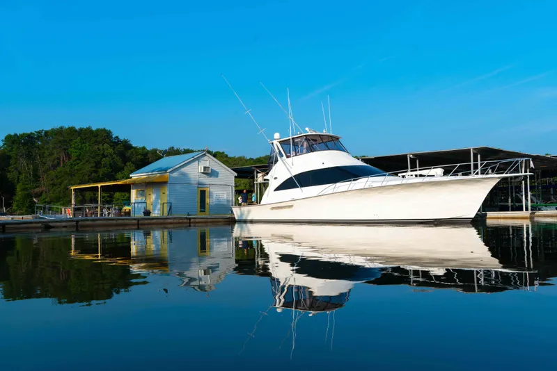 Slide: The Image of 1997 Ocean Yachts 60 Sport Fish docked by a serene lakeside cabin. - 12