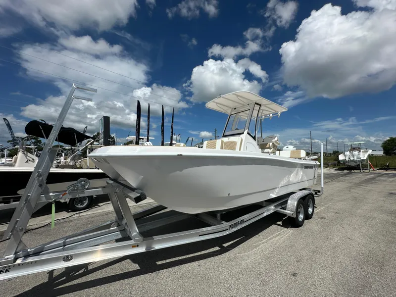Slide: The Image of 2026 Twin Vee 22 Bay Cat boat on trailer under a blue sky with clouds. - 2