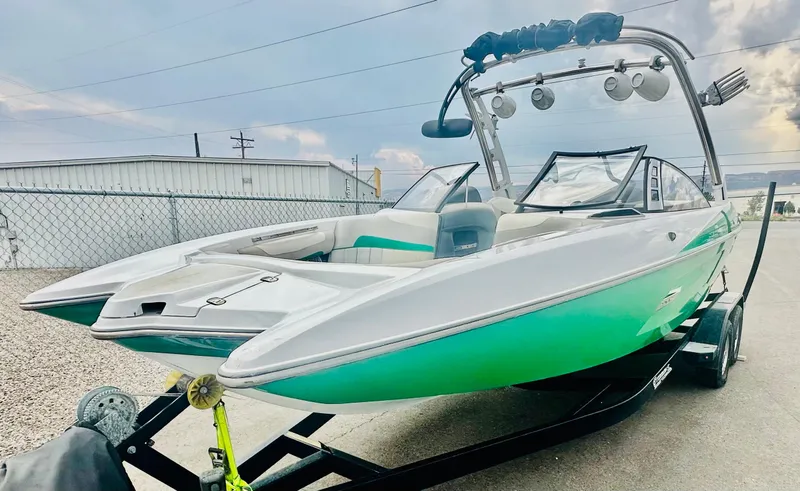 Slide: The Image of 2012 Malibu 22mxz boat on trailer, green and white exterior, parked outdoors. - 2