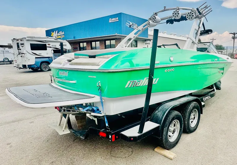Slide: The Image of 2012 Malibu 22mxz boat in vibrant green on a trailer, parked near a dealership. - 4