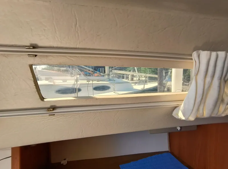 Slide: The Image of Interior view of a 1985 Catalina 27 sailboat, showing a window with a docked boat outside. - 29
