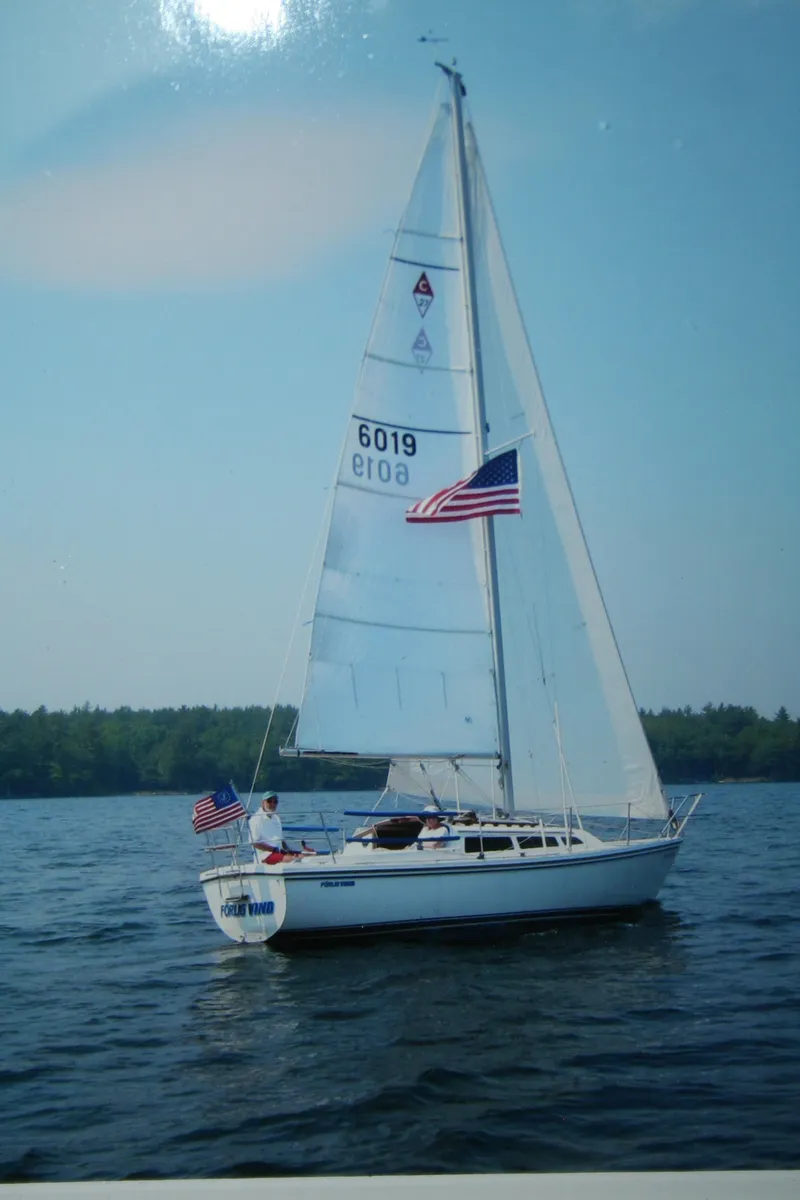 Slide: The Image of 1985 Catalina 27 sailboat on a lake with American flags, clear sky, and forested background. - 31